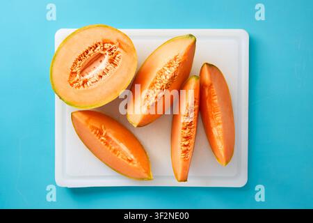 Fresh cantaloupe melon slices on a white cutting board over blue background. Healthy summer fruit. Stock Photo