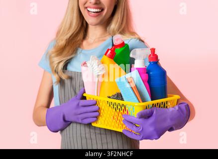 Focus on basket of cleaning supplies. Housewife in apron and purple rubber gloves Stock Photo