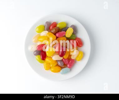 Jelly beans gummy candy pile on plate isolated. Chewing colorful marmalade pills, jelly gumdrops heap, gelatin jellybean candies set on white backgrou Stock Photo