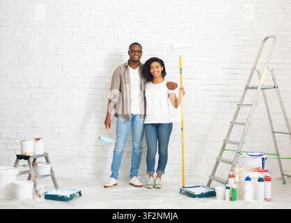Couple with repair tools and paint on white brick wall background Stock Photo