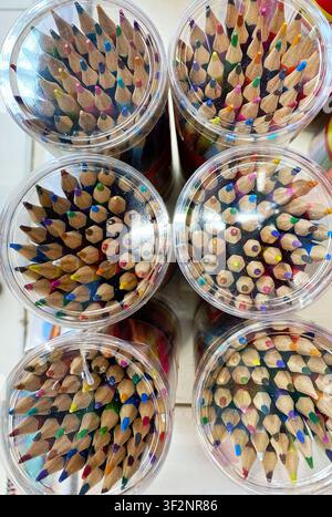 Wooden colored pencils in clear containers, featuring vibrant tips and arranged neatly, displayed on a white surface in a stationery shop Stock Photo