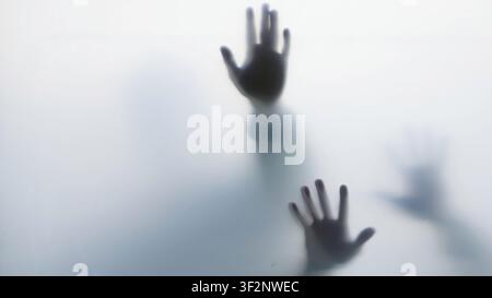 Dark hand silhouettes pressed against frosted glass Stock Photo