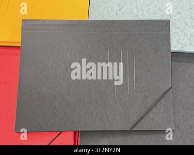 Black cardboard document folder with elastic closure placed on colorful office folders. Office stationery background for paperwork, organization Stock Photo