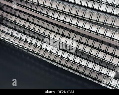 Close-up of stacked spiral bound notebooks with black wire rings and white paper edges. Repetitive stationery pattern for education, publishing Stock Photo