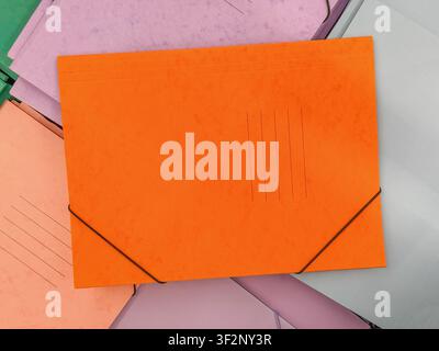 Bright orange cardboard document folder with elastic closure surrounded by pastel office folders. Colorful stationery composition for filing Stock Photo