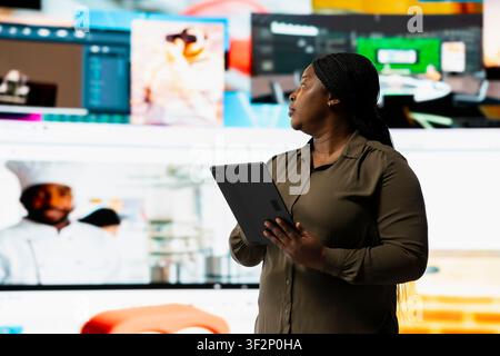 Person uses touchscreen tablet to stream online video content during leisure time in modern digital environment. Woman browses social media app in front of digital backdrop displaying clips collage Stock Photo