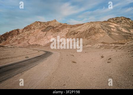 A paved road curves through eroded, mineral-banded Painted Canyon in Death Valley National Park. Layered hillsides in shades of tan, rust, and violet- Stock Photo