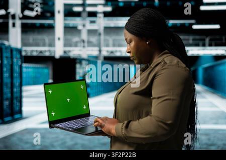 Developer holding isolated screen laptop walking through server room rows with storage mainframes. Computer scientist using mockup notebook to inspect data center helping power internet services Stock Photo