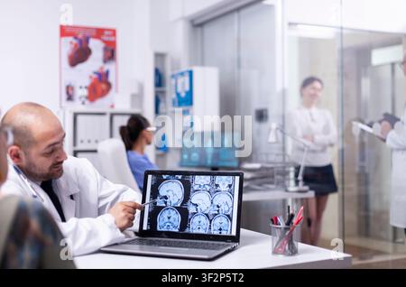 Woman speaking with doctor during consultation about cerebral xray using laptop in hospital, senior patient visiting physician telling health complaints. Stock Photo