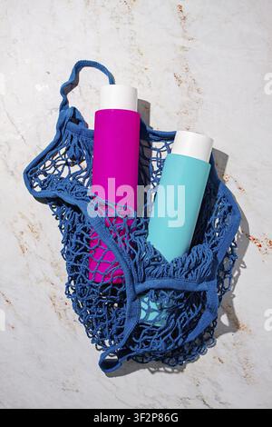 A net bag holds two bottles. One bottle is pink and the other is blue. The scene shows a light-colored surface underneath the bag Stock Photo