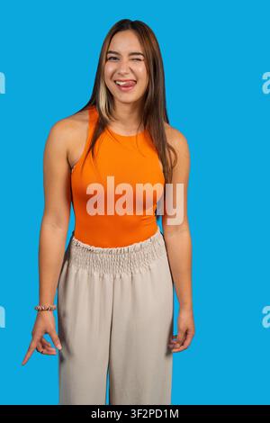 Young woman showing playful expression on blue background, gesturing with finger Stock Photo