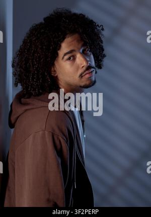 Young man wearing brown hoodie looking at camera with a thoughtful expression Stock Photo