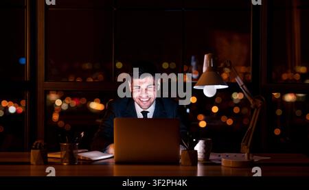 Smiling Businessman Working On Laptop At Workplace At Night Stock Photo