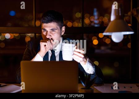 Business Man Yawning Working On Laptop Having Coffee In Office Stock Photo