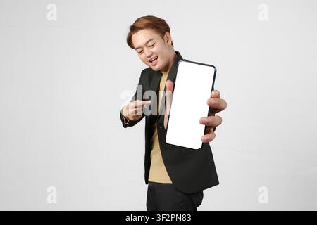 portrait of happy asian businessman wearing suit holding mobile phone and showing blank screen  with pointing finger gesture on isolated background Stock Photo