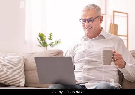 Elderly Man Using Laptop And Having Coffee Stock Photo