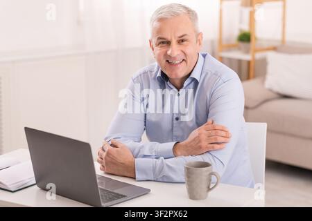 Senior man using laptop at office and looking at camera Stock Photo