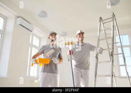 House painters standing in empty room near ladder preparing for painting the wall of new apartment. Stock Photo
