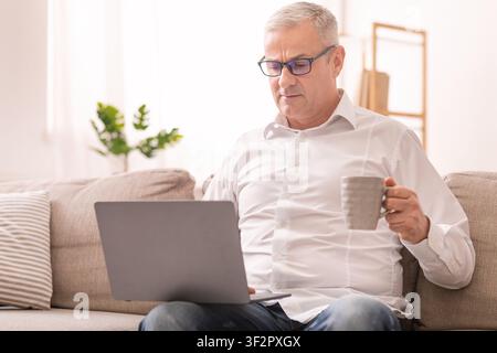 Elderly Man Using Laptop And Having Tea Stock Photo