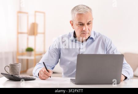 Serious senior man using laptop and writing Stock Photo