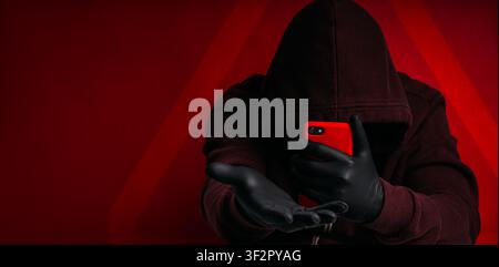 Cybercrime hacker using smartphone for online fraud and digital scam against victims. Anonymous cyber criminal in hoodie represents phishing, identity Stock Photo