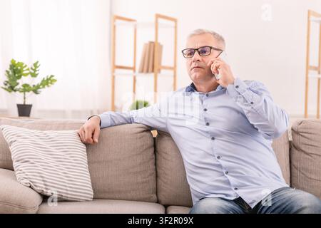 Serious mature man talking on mobile phone at home Stock Photo