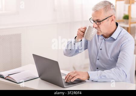 Happy senior man using laptop and drinking coffee Stock Photo