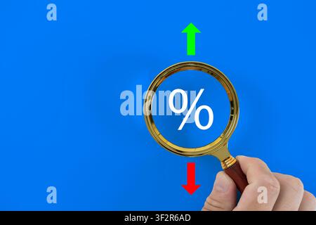 Interest rate and inflation concept. Magnifying glass with percentage sign, green up and red down arrows on blue background. Financial market fluctuat Stock Photo