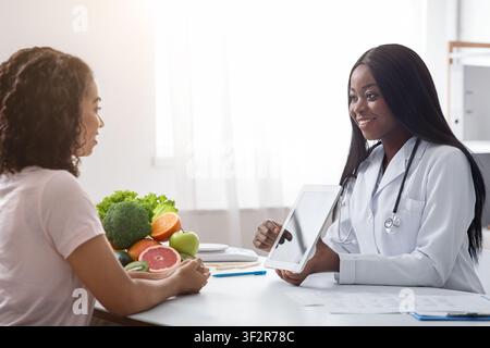 Woman nutritionist using digital tablet in office, consulting patient Stock Photo