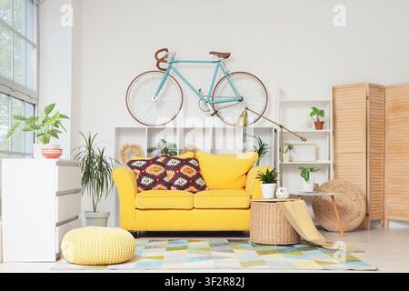 Bright yellow sofa with patterned pillows in a modern living room a bicycle mounted on the wall, a light blue bicycle is mounted on the white wall abo Stock Photo