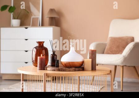 Aromatherapy diffuser with essential oil, reed diffuser, and lit candles on a wooden coffee table in a cozy living room Stock Photo