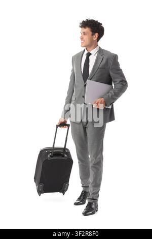 Smiling young businessman in a gray suit pulling a black rolling suitcase and holding a laptop isolated on white background Stock Photo