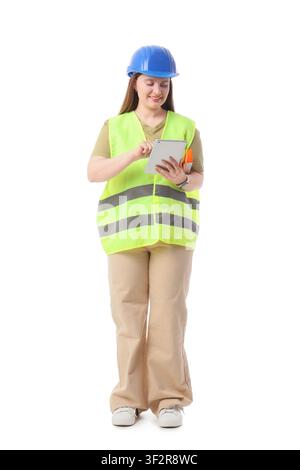 Female construction worker in a blue hard hat and safety vest using a digital tablet, isolated on white background, the professional woman stands full Stock Photo