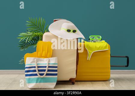 Summer vacation travel with packed suitcases, beach bag, hat, and snorkeling gear against a teal wall Stock Photo