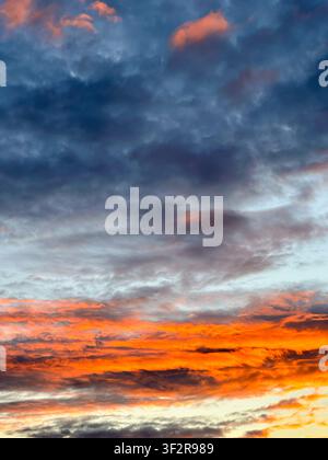 Vivid sunset sky featuring glowing orange clouds beneath dramatic dark storm clouds. A striking natural background ideal for weather, climate, nature, Stock Photo