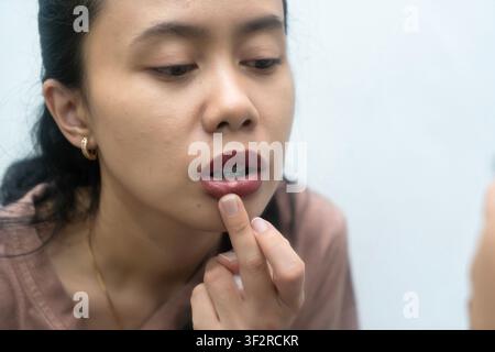 Asian Indonesian woman have canker sore on her lips. Looking at mirror Stock Photo