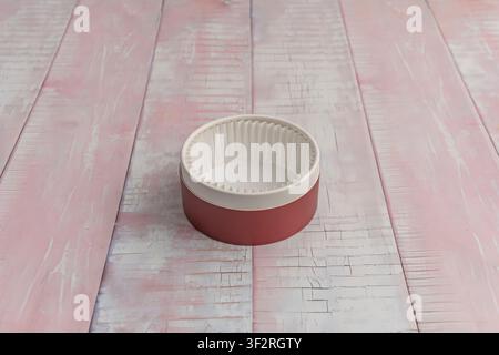 Empty Round Paper-Lined Container with Rustic Red Exterior on Weathered Pink Wooden Surface Stock Photo