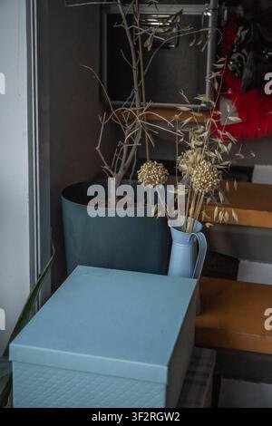Moody Corner Vignette Featuring Dried Branches and Allium Stems in a Pale Blue Pitcher Beside a Storage Box Stock Photo