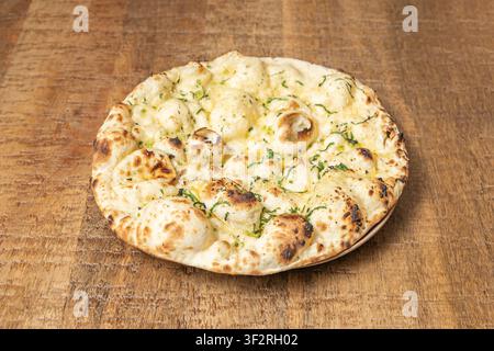 Low-angle shot of garlic naan bread highlighting puffy risen edges, herb flecks, and toasted char pattern on rustic wooden surface. Stock Photo