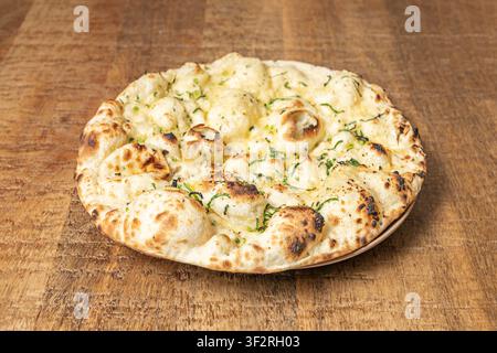 Low-angle shot of garlic naan bread highlighting puffy risen edges, herb flecks, and toasted char pattern on rustic wooden surface. Stock Photo