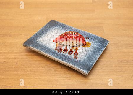 Single tuna nigiri glazed with dripping soy sauce and sesame seeds, plated on a speckled gray stone tray. Stock Photo