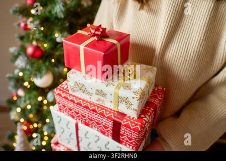 Woman holds wrapped Christmas gifts at home near a decorated tree with lights and ornaments. Concept of holiday presents and Christmas celebration. Stock Photo