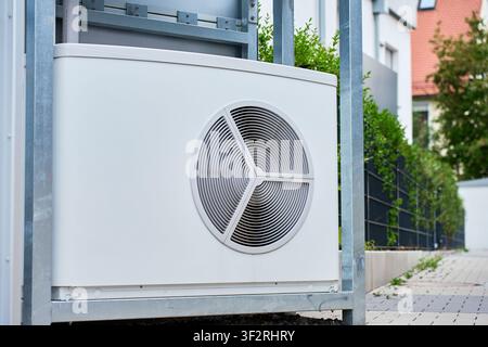 White heat pump unit with circular fan grille on galvanized steel mounting frame near residential building Stock Photo