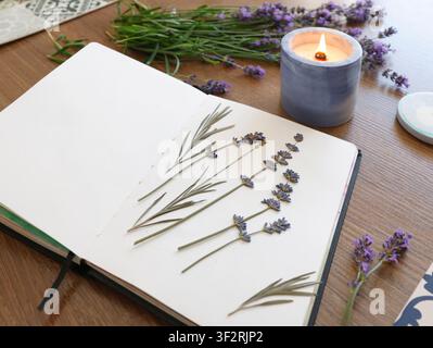 Opened blank notebook with dried lavender herbarium on white paper near burning soy candle for mindful journaling and creative hobby inspiration. Stock Photo