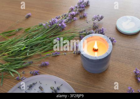 High angle view of aromatic soy candle burning on wooden desk next to fresh lavender flowers bouquet for mindful self care routine web banner design. Stock Photo