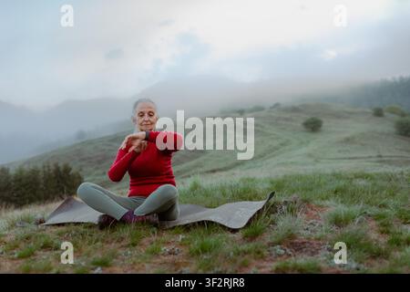 Senior woman checking her performance after exercise in nature on early morning. Stock Photo