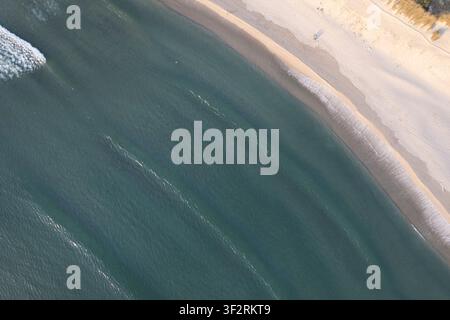 Relaxing evening scene at the seashore featuring deep water and pristine sand seen from a drone Stock Photo