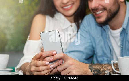 Unrecognizable Couple Using Smartphone Sitting In Cafeteria, Cropped Stock Photo