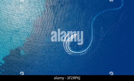 Drone view over blue waters near Kallithea reveals a white boat wake curving into a circular spiral across the surface of water. Stock Photo