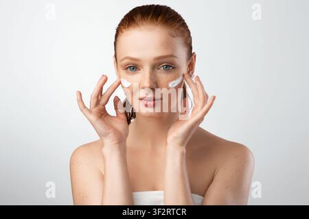 Young Female Applying Face Cream With Both Hands, Studio Shot Stock Photo